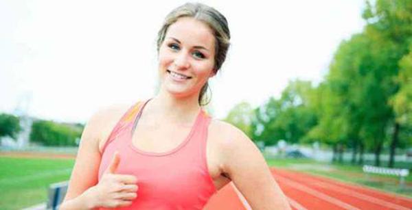 Girl smiling and thumbs up in front of a track field